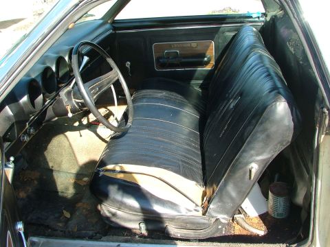 1969 Ford Ranchero - The interior of a 1969 Ford Ranchero features a worn black bench seat and a dashboard with three gauges visible.