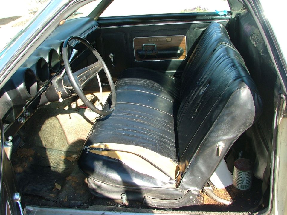 Worn black bench seat and dash interior of an old car with torn upholstery