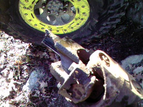 1976 GMC C/K Pickup - A close-up view of a damaged suspension component lying on the ground next to a large tire with a yellow rim.