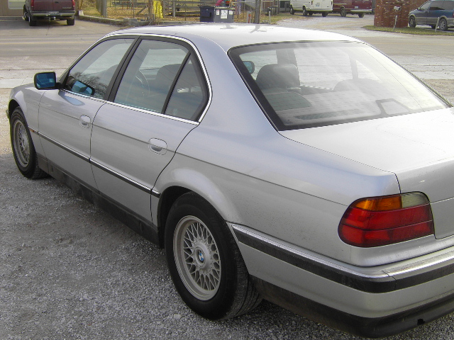 Silver BMW sedan rear three-quarter view parked on gravel
