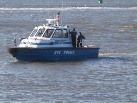 1991 Ford LTD Crown Victoria - A New York City Police boat cruises on the water, identified by the text on its hull.