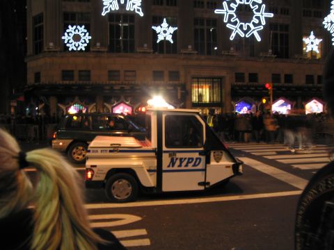 1991 Ford LTD Crown Victoria - A small NYPD electric vehicle drives down a street decorated with snowflake lights.