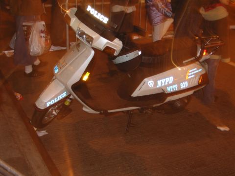 1991 Ford LTD Crown Victoria - A white police scooter with NYPD markings is parked on a street at night.