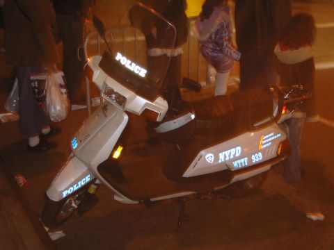 1991 Ford LTD Crown Victoria - A police scooter marked "POLICE" and "NYPD MTTF 939" is parked on a street at night.