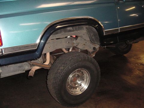 1984 Ford Bronco - The rear tire and suspension components are visible, along with the exhaust pipe exiting the vehicle.
