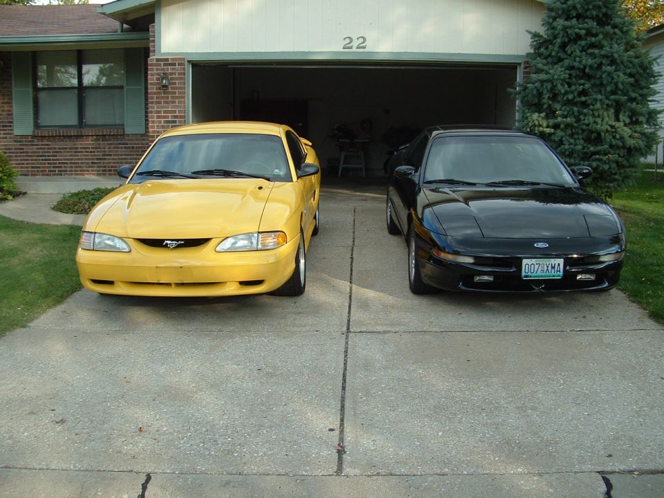 Yellow Ford Mustang and black Ford Probe parked in front of a garage