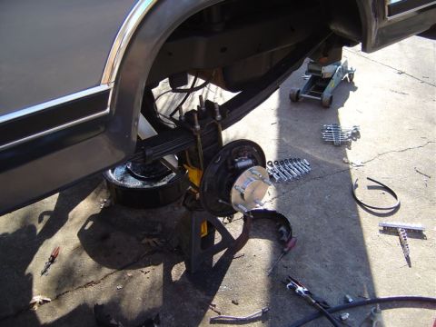 1986 Ford Bronco - The rear brake assembly of a vehicle is shown disassembled on a concrete surface with tools scattered around.