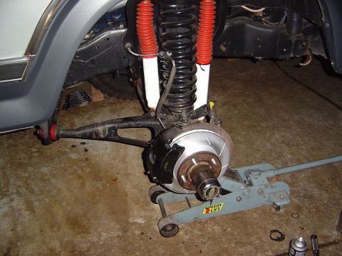 1986 Ford Bronco - Front suspension of a lifted truck with the wheel removed, showing a new slotted brake rotor and caliper on the spindle, a coil spring with…