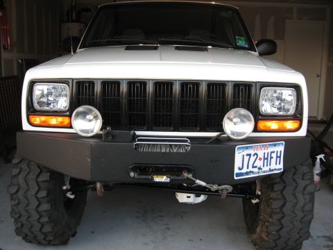 1986 Ford Bronco - This white Jeep Cherokee features a black grille, auxiliary lights, and a heavy-duty aftermarket bumper with a winch.