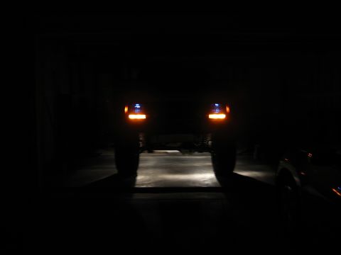 1986 Ford Bronco - Rear view of a dark SUV with illuminated tail lights. Another vehicle is partially visible on the right.