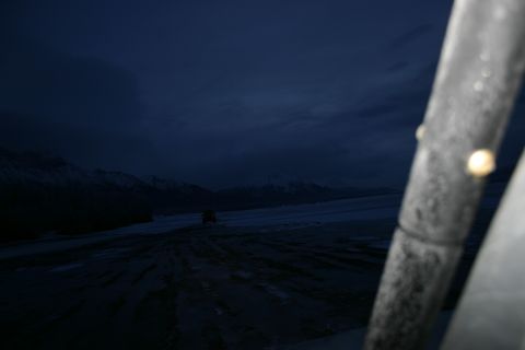 2003 Jeep TJ - A red vehicle travels across a snow-covered landscape under a dark, cloudy sky, with mountains visible in the distance.