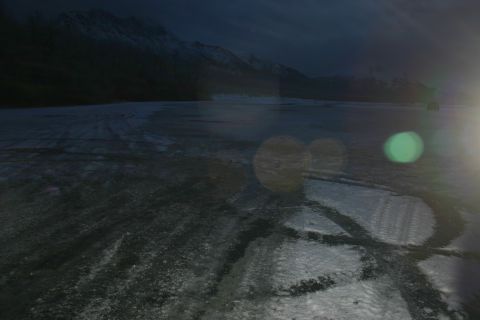 2003 Jeep TJ - A vehicle is barely visible in the distance on a vast, icy plain with snow-capped mountains under a dark sky.