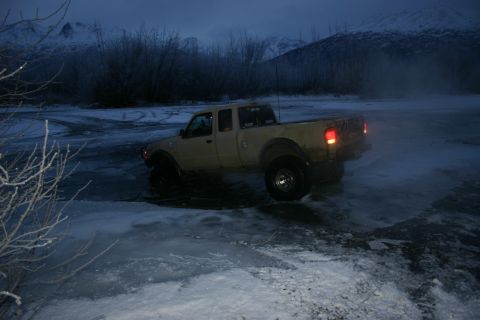 2003 Jeep TJ - A tan pickup truck navigates icy terrain in a dimly lit, snowy landscape.