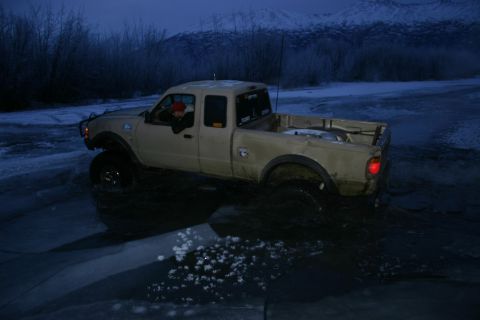 2003 Jeep TJ - Pickup truck navigates icy terrain with a snowy mountain range behind it.