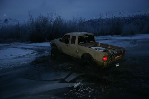 2003 Jeep TJ - A tan pickup truck navigates a muddy, icy path in a cold, remote landscape.