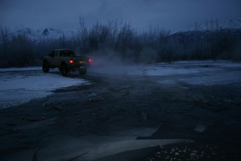 2003 Jeep TJ - A truck drives on a snowy road at dusk, with mountains in the background.