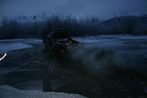 2003 Jeep TJ - A pickup truck navigates through a frozen waterway, creating a spray of water and ice.