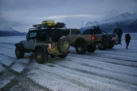 2003 Jeep TJ - Several off-road vehicles are parked on a snow-covered road, with a person walking away from the camera.