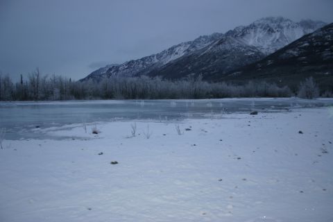 2003 Jeep TJ - A winter scene unfolds with snow-dusted trees and a partially frozen lake before imposing, snow-capped mountains.