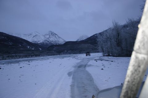 2003 Jeep TJ - A lone SUV navigates a snowy path through a valley, with snow-capped mountains looming in the distance under a cloudy sky.