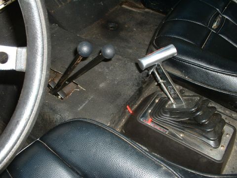 1995 Ford Bronco - The interior of a vehicle features a steering wheel and multiple gear shifters, indicating a manual transmission setup.