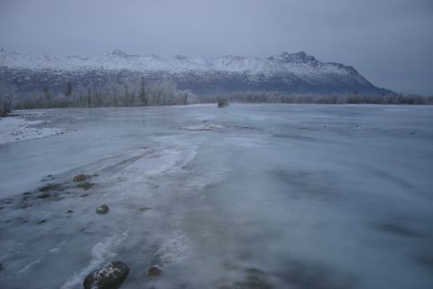 2003 Jeep TJ - A Jeep navigates a frozen expanse under a cloudy sky, with snow-capped mountains looming.