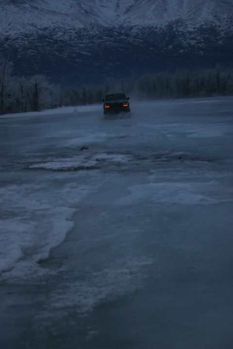 2003 Jeep TJ - An SUV navigates through a partially frozen body of water during twilight, with snow-capped mountains visible in the distance.