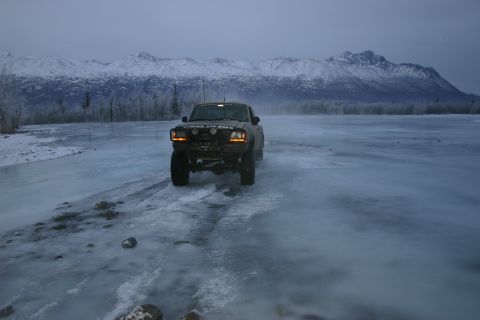2003 Jeep TJ - A black pickup truck navigates an icy landscape with snow-capped mountains in the background.