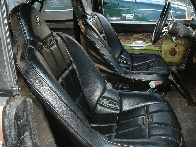 Black bucket seats inside a vehicle, with a green Ford F-150 visible through the window