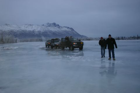2003 Jeep TJ - Trucks traverse a frozen landscape under a cloudy sky, with mountains in the distance.