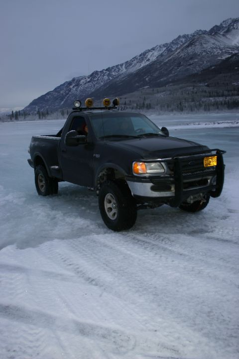 2003 Jeep TJ - A black Ford F-150 pickup truck is parked on a frozen surface with snow-covered mountains in the distance.