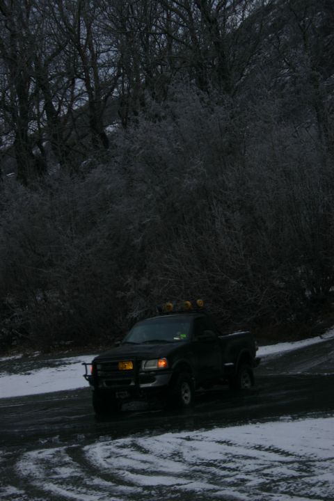 2003 Jeep TJ - Pickup truck driving on a snowy road with trees in the background.