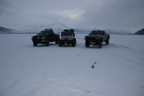 2003 Jeep TJ - Three off-road vehicles are parked in a wide, snow-covered area with mountains visible in the distance under an overcast sky.