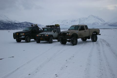 2003 Jeep TJ - Three off-road vehicles, including a 2003 Jeep TJ, are parked in a snowy area with mountains in the background.