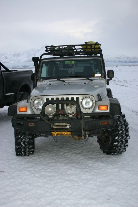 2003 Jeep TJ - A silver 2003 Jeep TJ equipped with a roof rack and winch is parked in a snowy landscape, with another vehicle partially visible to the lef…