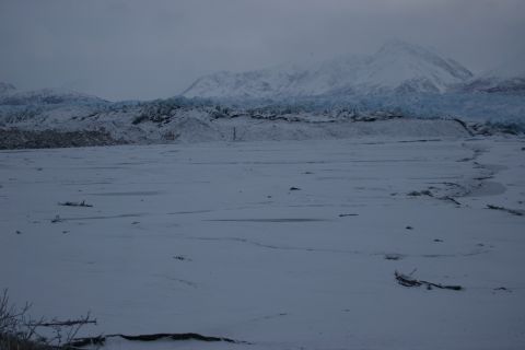 2003 Jeep TJ - A vast, snow-covered plain stretches towards a distant glacier and snow-capped mountains under an overcast sky.