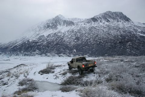 2003 Jeep TJ - Pickup truck navigates snowy terrain with a mountain range in the background.