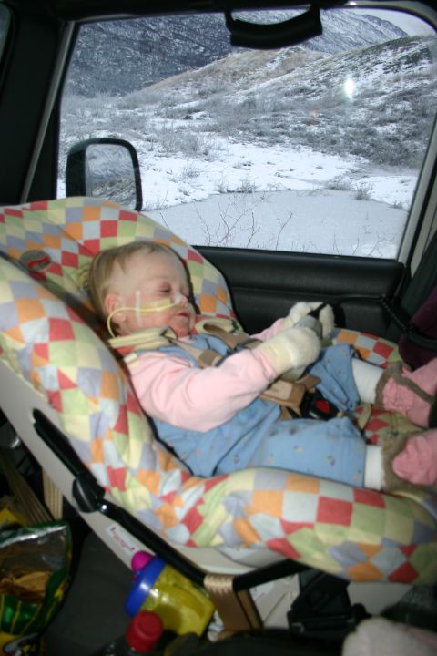 2003 Jeep TJ - A child in a car seat, with medical tubing, is transported through a snowy landscape.