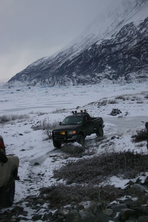 2003 Jeep TJ - A pickup truck navigates a challenging snowy path near a glacier under an overcast sky.