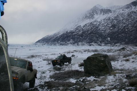 2003 Jeep TJ - Two pickup trucks navigate a snowy terrain with a vast glacier and imposing mountains in the distance.