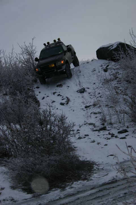 2003 Jeep TJ - A black pickup truck navigates a steep, snow-covered incline with sparse vegetation.