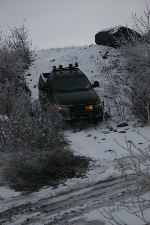 2003 Jeep TJ - A black pickup truck navigates a snowy incline, its roof lights illuminating the path ahead. The license plate appears to indicate the year…