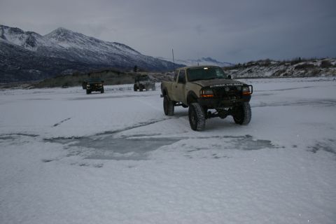 2003 Jeep TJ - Several off-road trucks traverse a frozen landscape under a cloudy sky, with snow-capped mountains in the distance.
