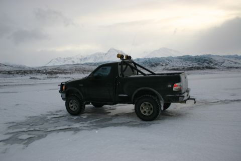 2003 Jeep TJ - A black pickup truck is parked on a frozen surface with a dramatic mountain and glacier landscape behind it.