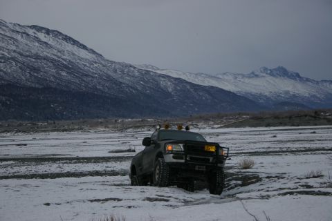 2003 Jeep TJ - A dark 2003 Jeep TJ navigates a snowy, rocky landscape with snow-capped mountains looming behind.