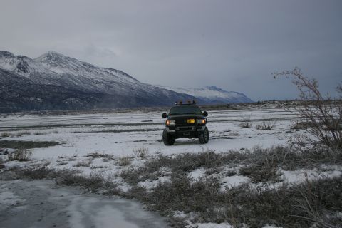 2003 Jeep TJ - A black SUV is parked in a snow-covered field with mountains in the distance under an overcast sky.
