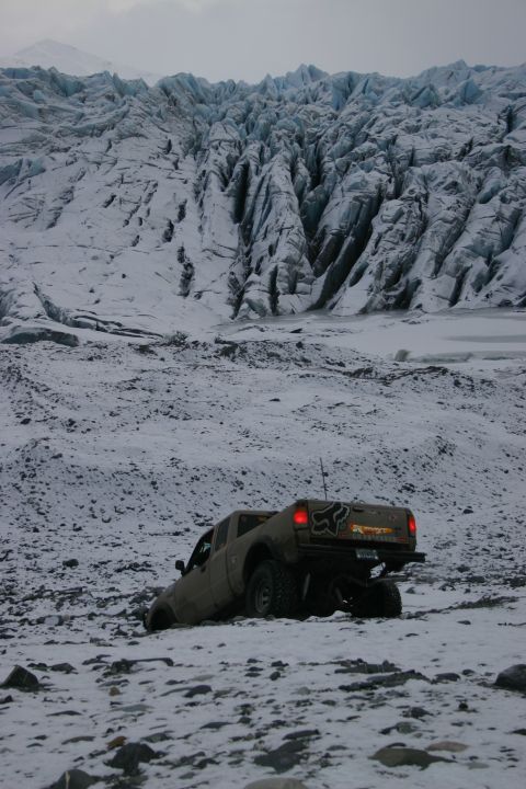 2003 Jeep TJ - A tan pickup truck navigates a snowy, rocky landscape with a massive glacier visible in the background.