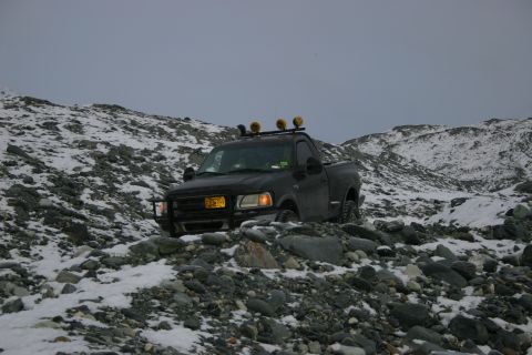 2003 Jeep TJ - A black pickup truck navigates a rocky, snow-covered terrain under an overcast sky.