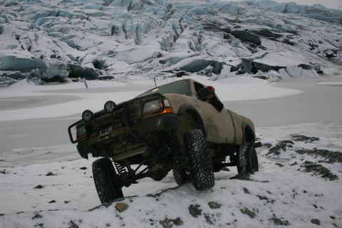 2003 Jeep TJ - A tan pickup truck navigates snowy terrain with a large glacier in the background.