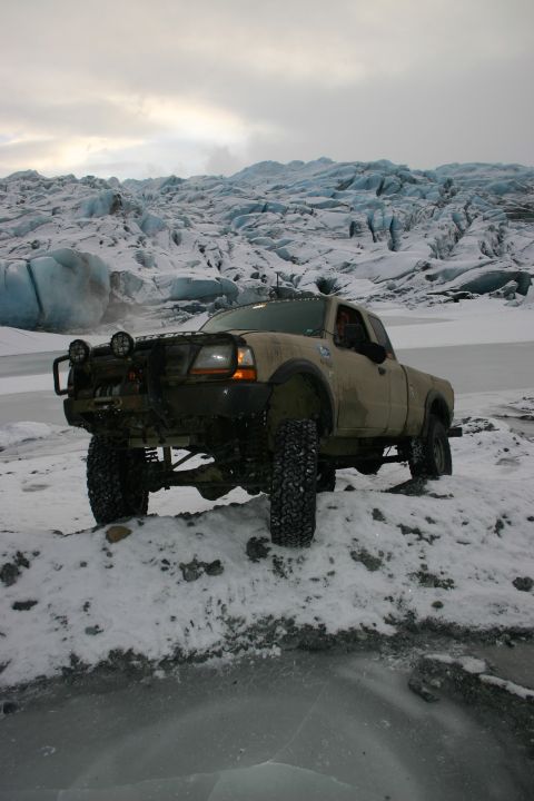 2003 Jeep TJ - A tan pickup truck navigates a snowy and icy environment with a glacier visible in the background.